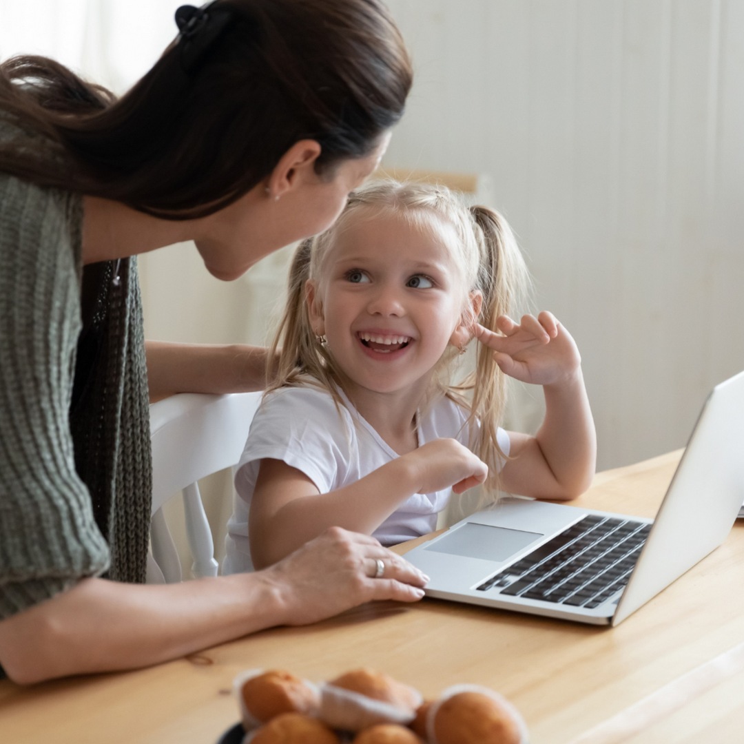 Imagen de portada de curso "Pensamiento computacional en el Nivel Inicial" - Se visualiza una Nena sonriendo y mirando a una Mujer indicando algo en la pantalla de una notebook