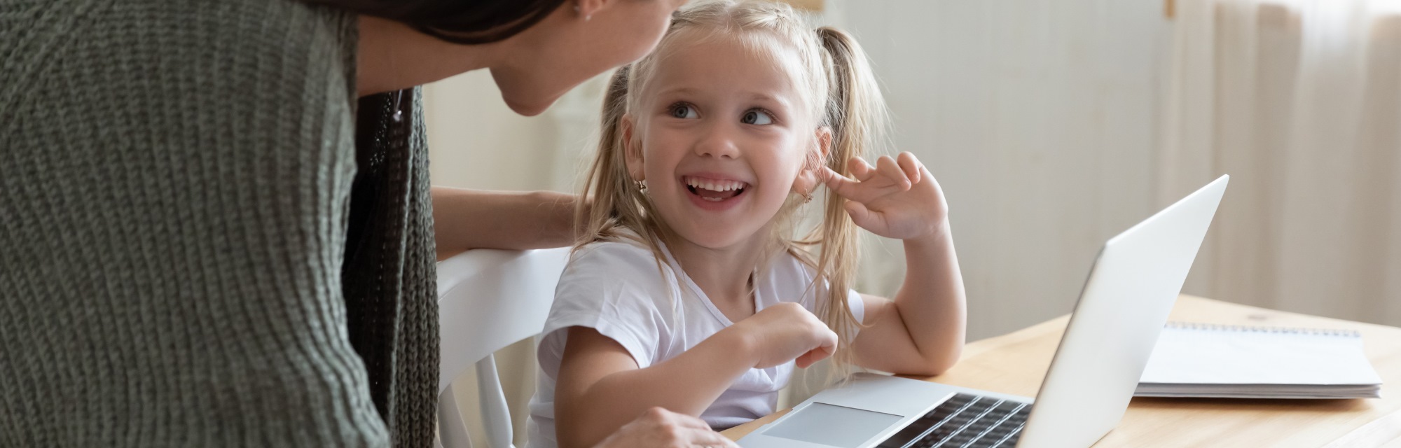 Imagen de portada de curso "Pensamiento computacional en el Nivel Inicial" - Se visualiza una Nena sonriendo y mirando a una Mujer indicando algo en la pantalla de una notebook
